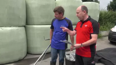 2 mens in front of wrapped balers