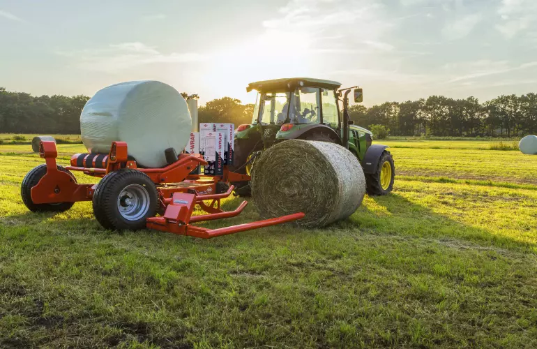 RW 1610 bale trailed round bale wrapper loading a round bale during wrapping of another bale.