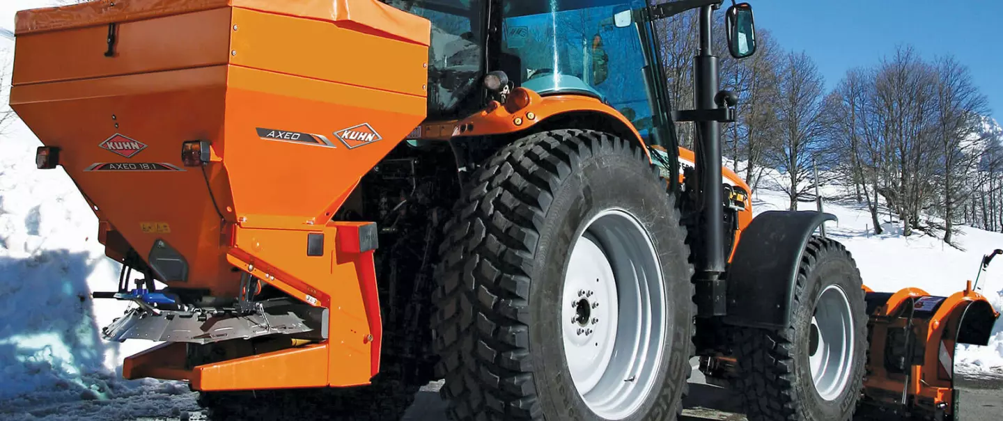 AXEO zout-, zand-, grind- en kunstmeststrooier aan het werk op een besneeuwde weg in de bergen met een skiër