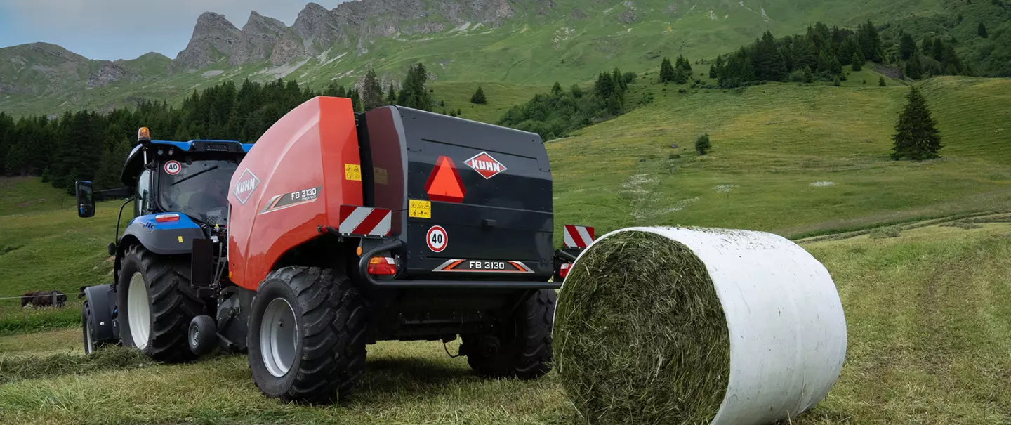 Presse à balles rondes à chambre fixe KUHN FB 3130 avec liage par film produisant des balles rondes en montagne.