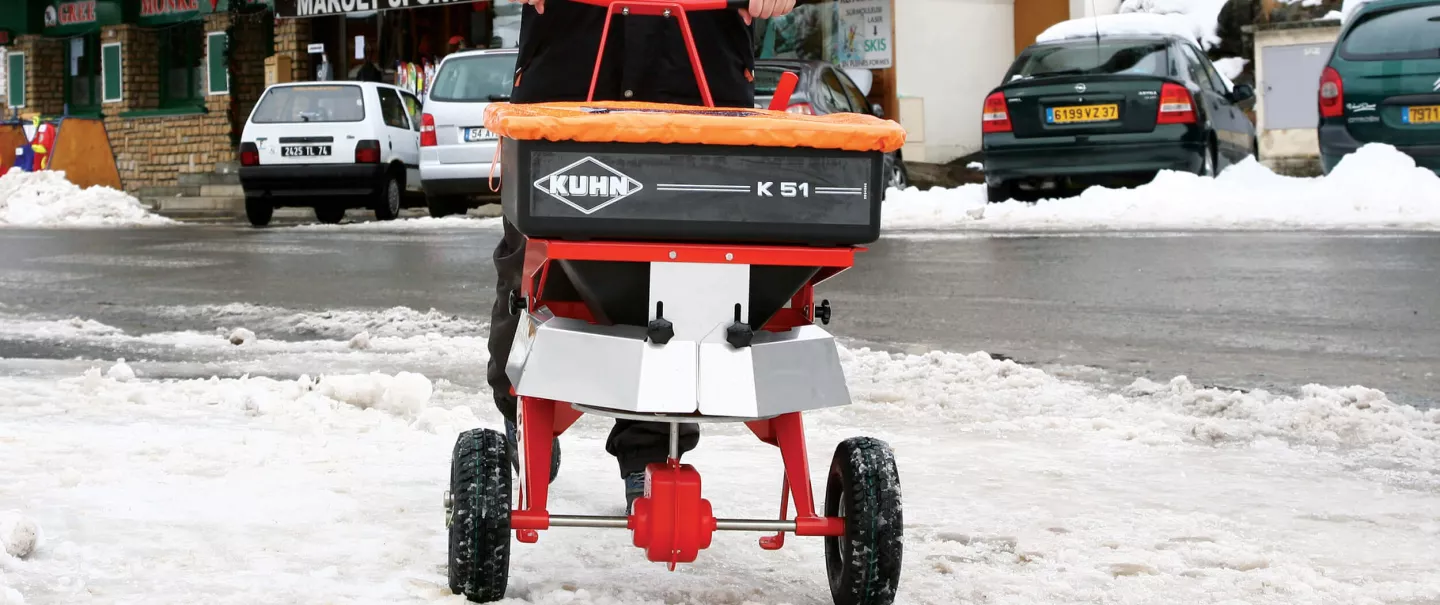 Carretilla distribuidora de empuje K51 con sal y arena en acción en invierno en la nieve