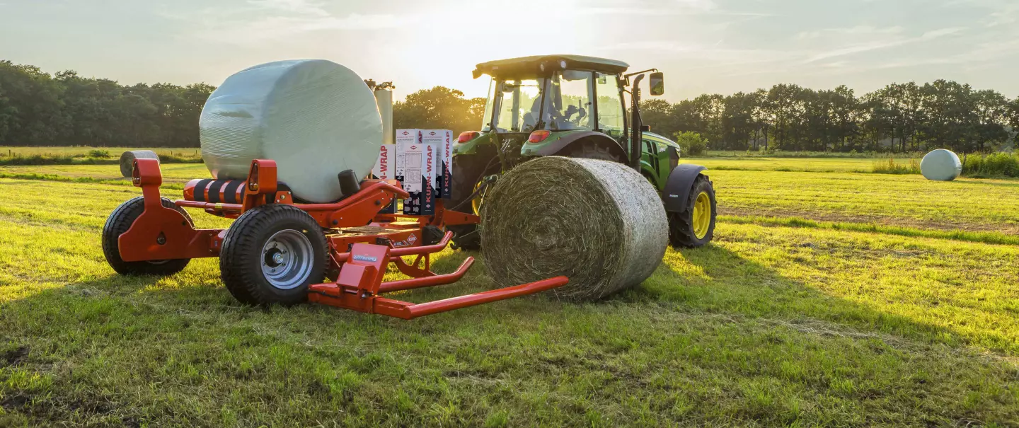 Encintadora de pacas redondas remolcada RW 1610 cargando una paca redonda mientras encinta otra paca.