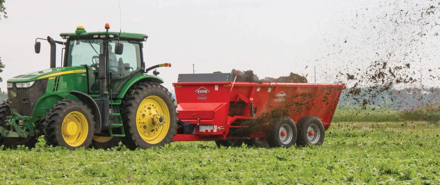 Side view of a SL 124 manure spreader spreading in a hay field.