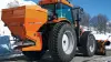 AXEO salt, sand, gravel and fertiliser spreader at work on a mountain road in the snow with a skier