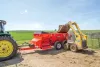 A skid loader is dumping a bucket of manure into a SL 124 manure spreader.